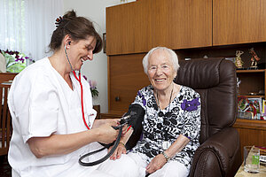 Pflegerin misst Seniorin in ihrem Wohnzimmer den Blutdruck