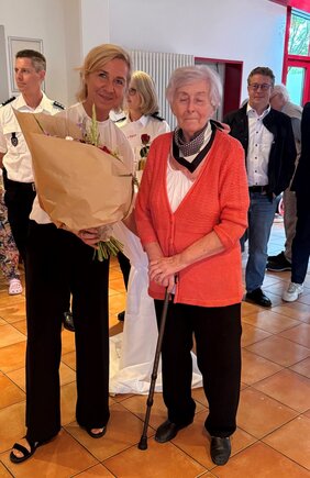 Beatrix Müller (Seniorenbetreuerin) überreicht Frau Nieder einen Blumenstrauß. Sie ist bereits seit 50 Jahren im MBH tätig.